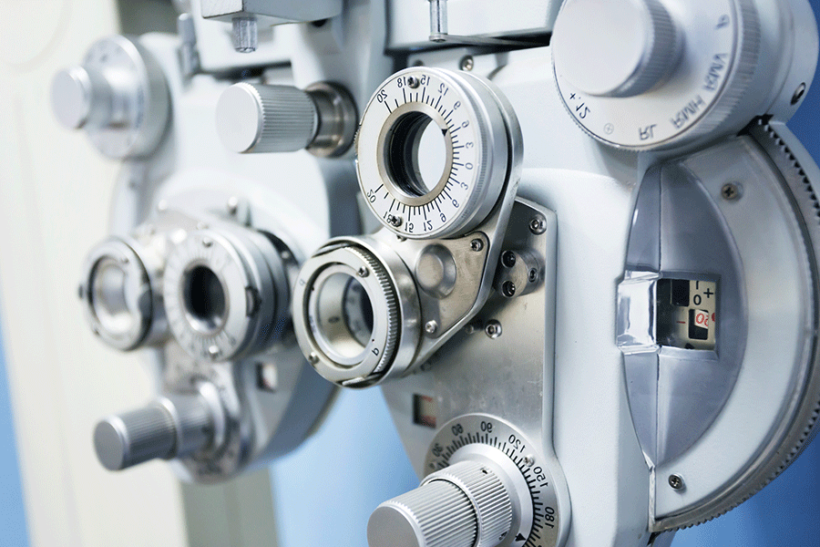 A close-up photo of optometry equipment, including an ultramatic RX master phoropter used for refraction of the eye. The machine is white and silver and has assorted dials and lenses.  